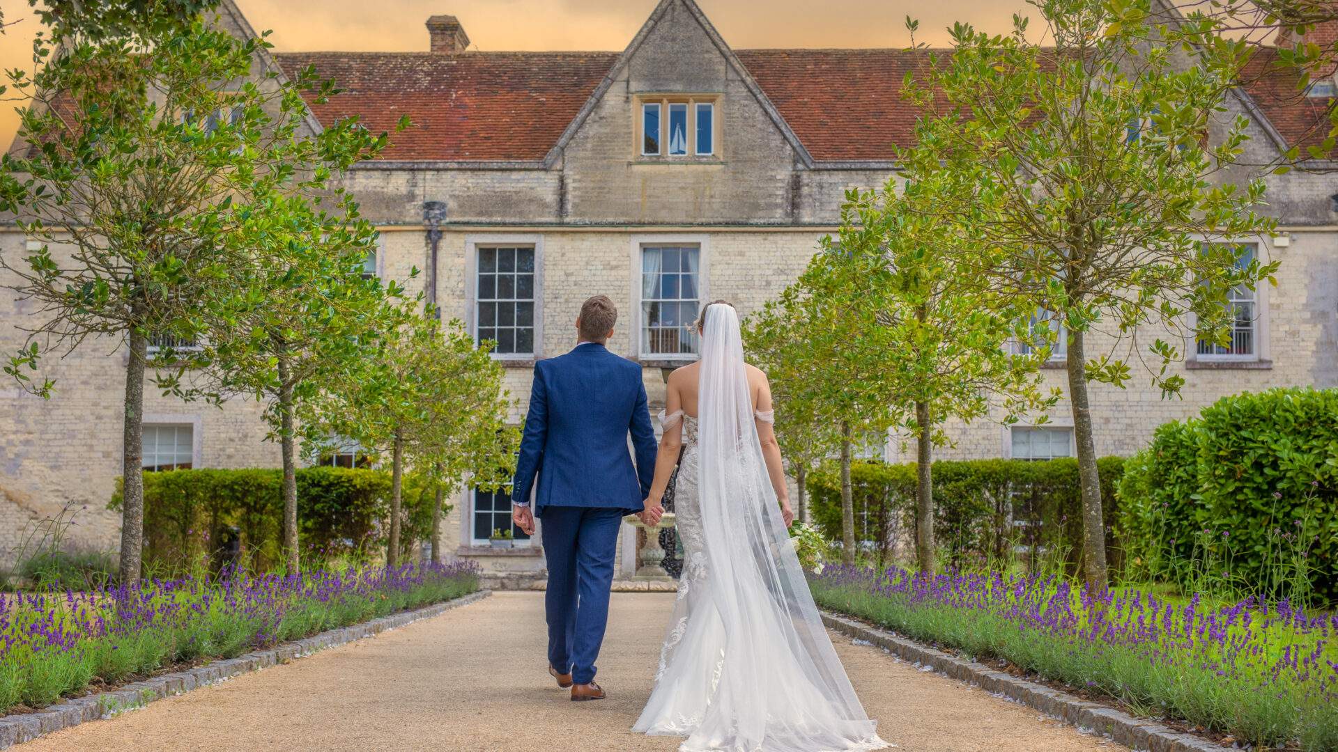 A couple walking down the grand tree lined entrance at Froyle Park, an exclusive use wedding venue in Hampshire