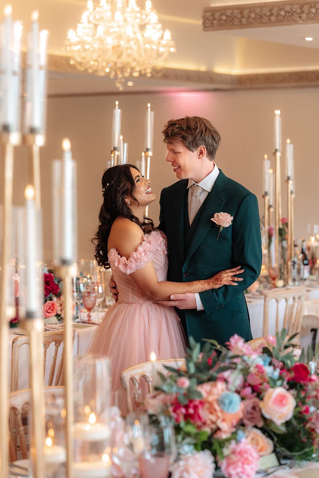 a bride in a fairytale pink gown and her groom in emerald green tux, stand in the beautifully decorated ballroom at Froyle Park