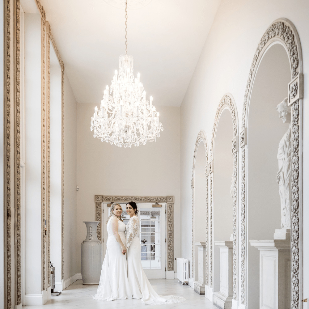 Two Brides pose in the stunning Ballroom Walkway following their wedding ceremony at Froyle Park