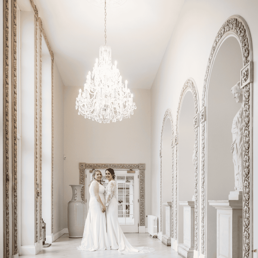 Two Brides pose in the stunning Ballroom Walkway following their wedding ceremony at Froyle Park