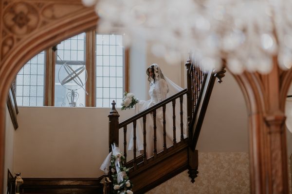 A bride makes her entrance down the grand staircase into the Great Hall at Froyle Park wedding venue in Hampshire