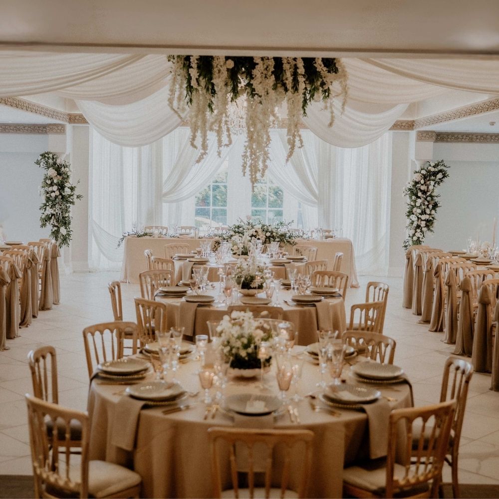 A wedding breakfast setup featuring beautiful white draping and a floral chandelier at Froyle Park wedding venue in Hampshire